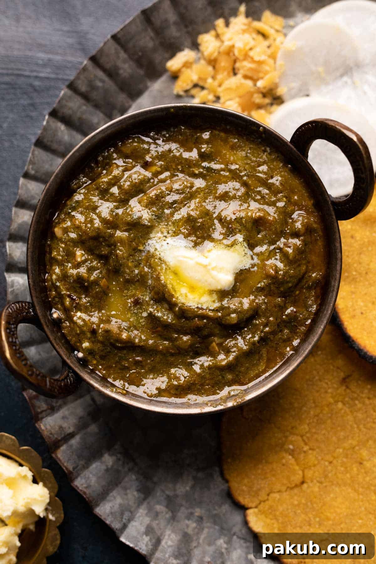 Authentic Punjabi Sarson Ka Saag 2 Picture of sarson ka saag served in a small copper kadhai with makki roti on the side