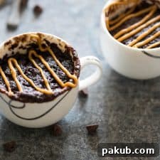 A cozy eggless banana chocolate peanut butter mug cake, served in a teacup and topped with extra peanut butter.