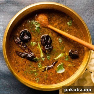 Picture of rasam in the brass pot that it was cooked in with a wooden ladle and some papad on the side