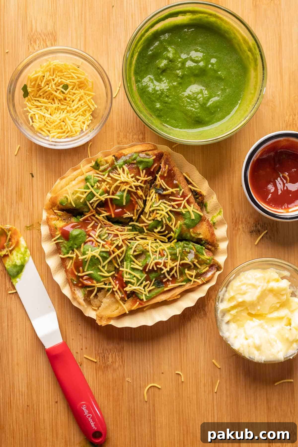 Mumbai Street Toastie 2 Crispy Bombay Sandwich Toast topped with butter, green chutney, ketchup, and sev, served on a paper plate, ready to be enjoyed.