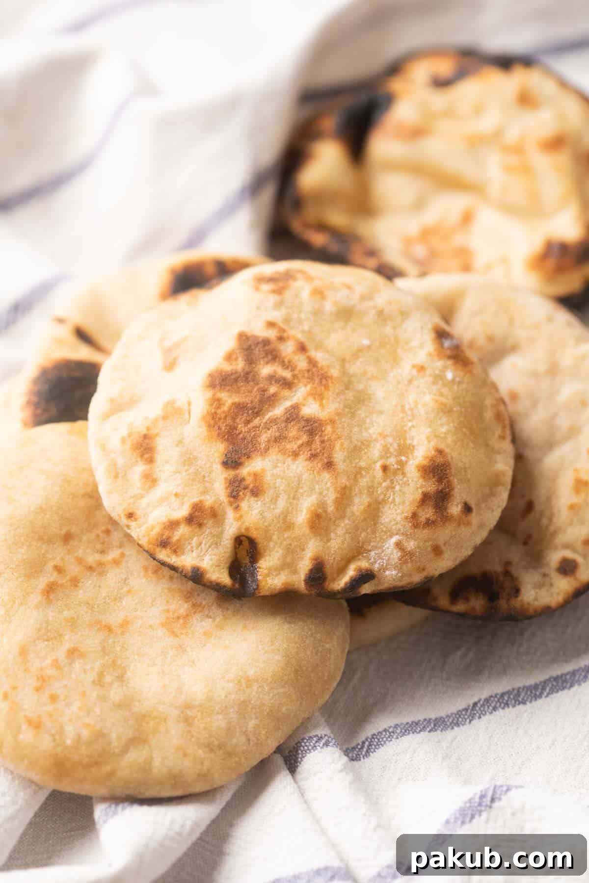 Simple Wholesome Whole Wheat Pita 7 Picture of Whole wheat pita breads kept on a striped white kitchen cloth, golden brown and puffed