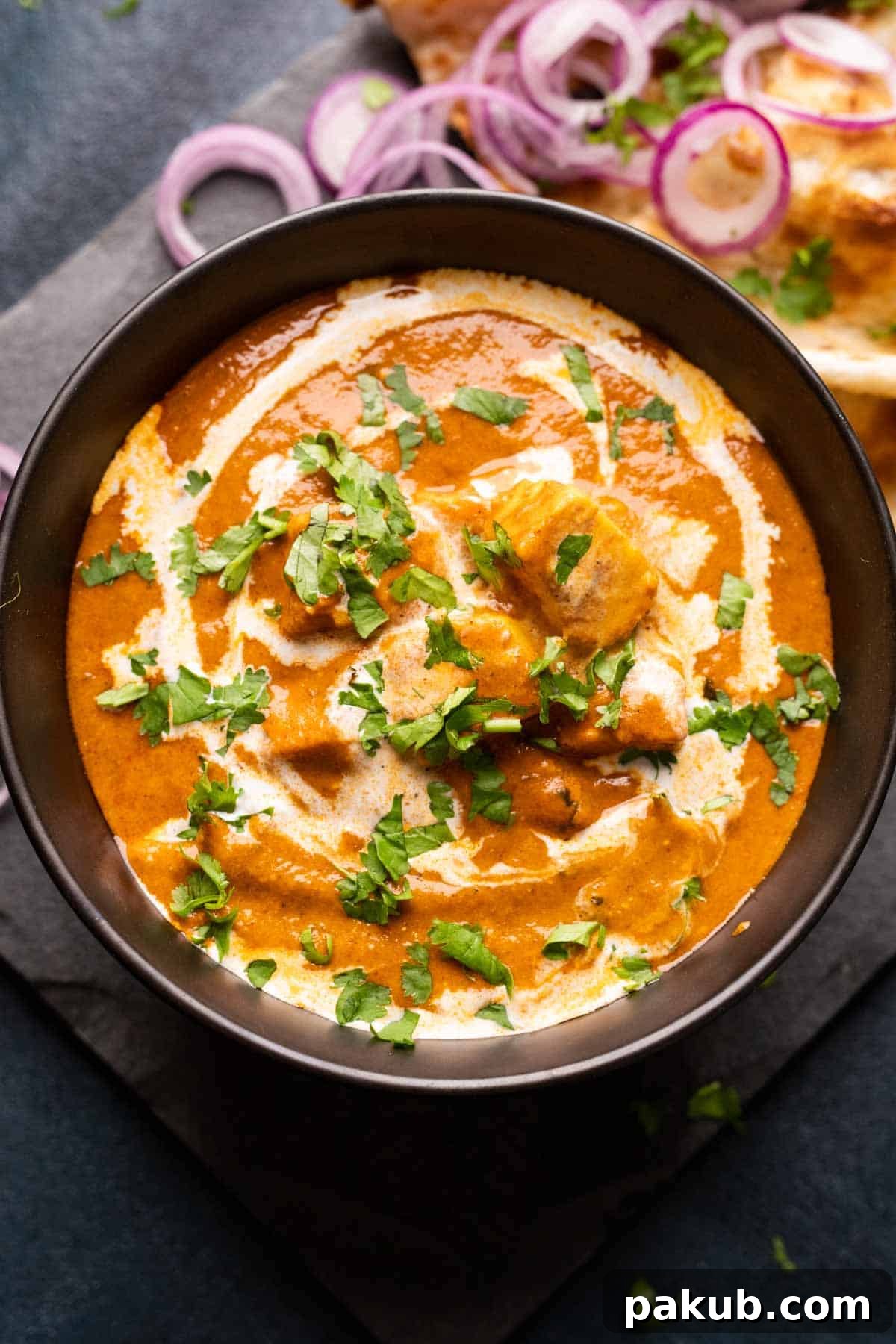 Shahi Paneer The Royal Indian Delight 2 Picture of shahi paneer served in a black bowl with onions and naan on the side, highlighting its rich texture and vibrant color.