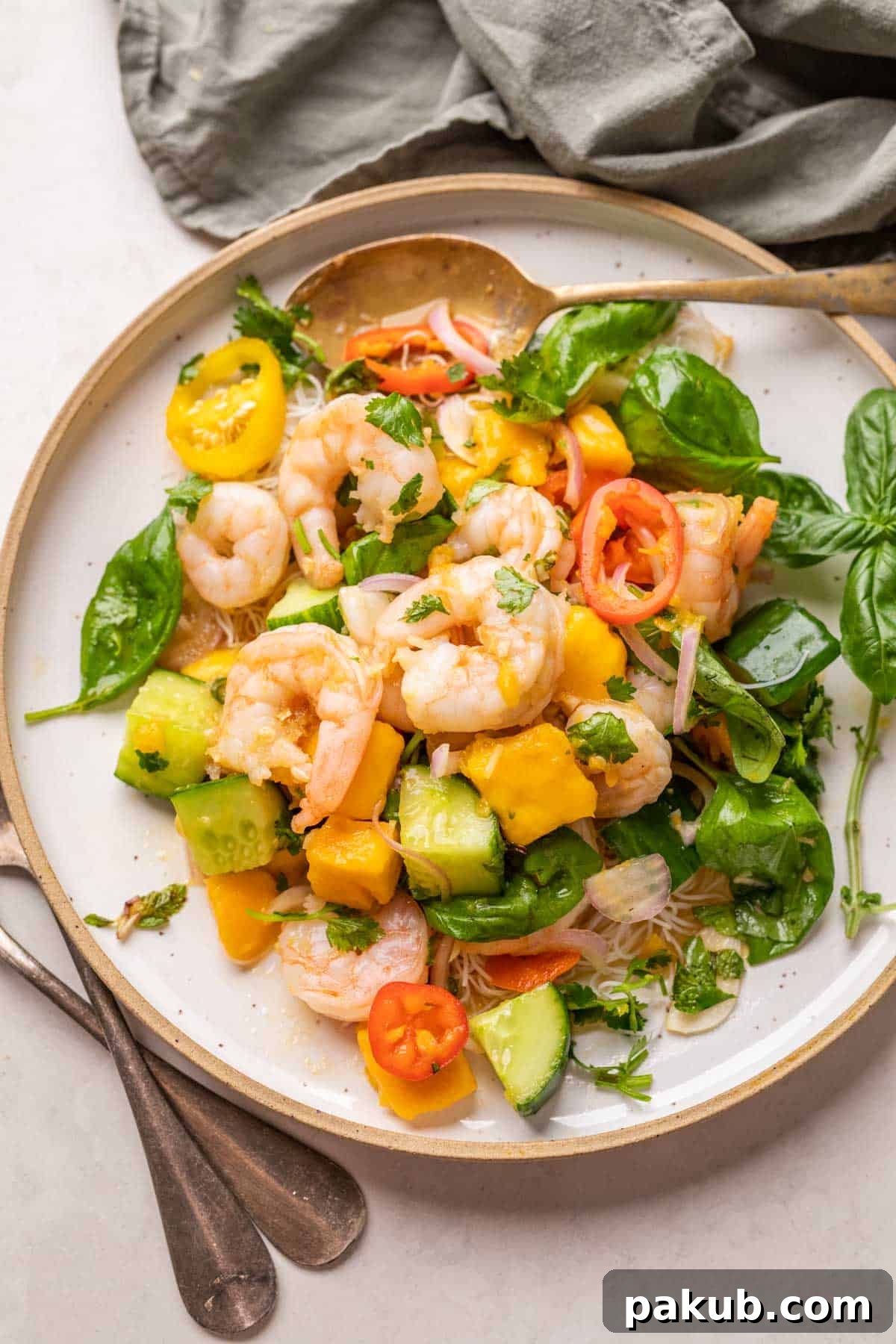 Beautifully plated Thai Prawn Mango Salad with juicy prawns, ripe mango, fresh herbs, and crisp vegetables, served with elegant cutlery.