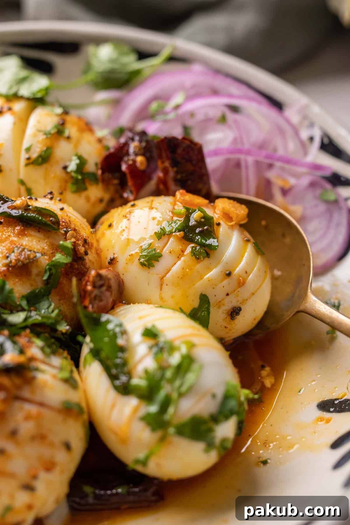 Close up of hasselback egg tadka with a spoon and sliced onions on the side