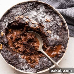 A spoon digging into an eggless chocolate pudding cake, revealing the rich chocolate sauce at the bottom.
