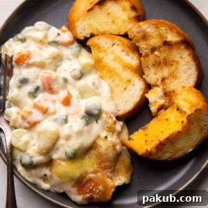 A serving of creamy Veg Au Gratin, topped with golden-brown cheese, accompanied by garlic bread slices.