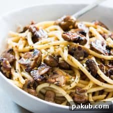 Delicious mushroom spaghetti aglio olio garnished with Parmesan cheese in a white bowl.