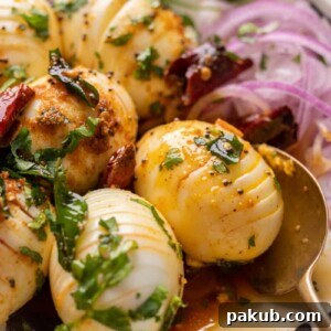 Close-up of hasselback egg tadka with a spoon and sliced onions, highlighting the intricate cuts.