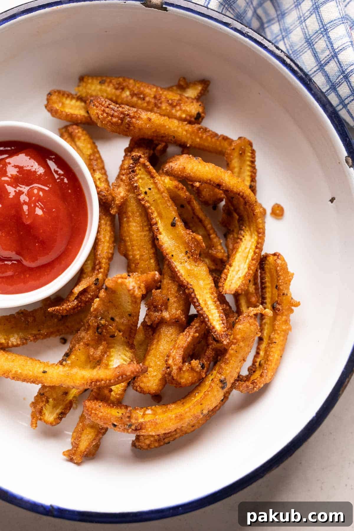Irresistible Baby Corn Crisps 8 Crispy baby corn fry served artfully in a white bowl with a vibrant red dipping sauce on the side