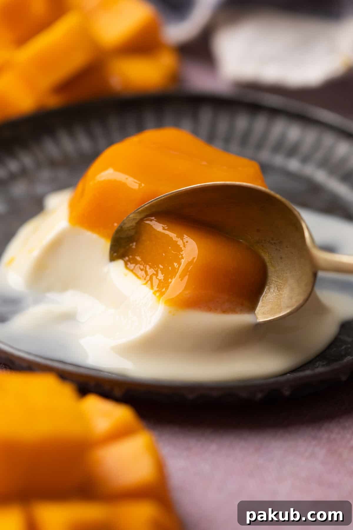 A spoon taking out a bite off the mango panna cotta, showcasing its creamy and jelly layers