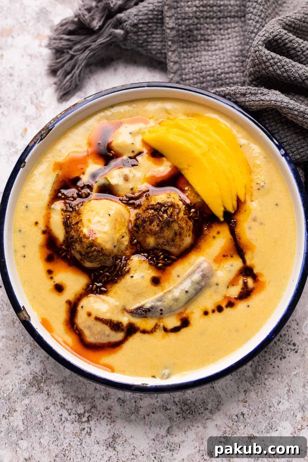 A vibrant bowl of Mango Kadhi, garnished with fresh mango slices and a rich tempering of spices, ready to be served.