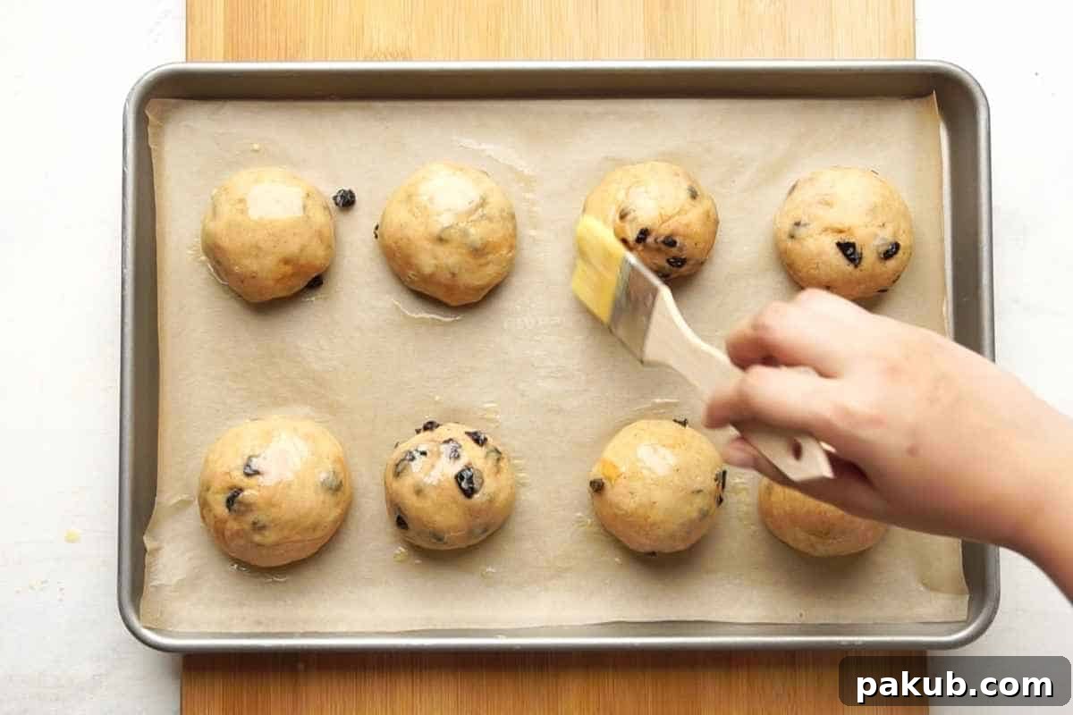 Homemade Bread Made Easy 8 A hand gently brushing a milk or egg wash over the shaped dough balls resting on parchment paper in a baking pan, prior to baking