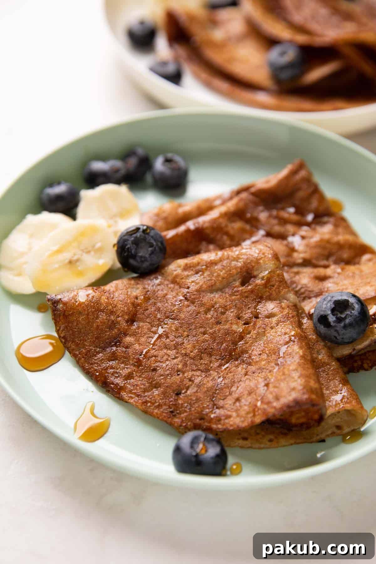 Close up of healthy banana dosa served on a vibrant green kids plate, garnished with fresh banana slices and a drizzle of honey, showcasing its appealing golden-brown texture.