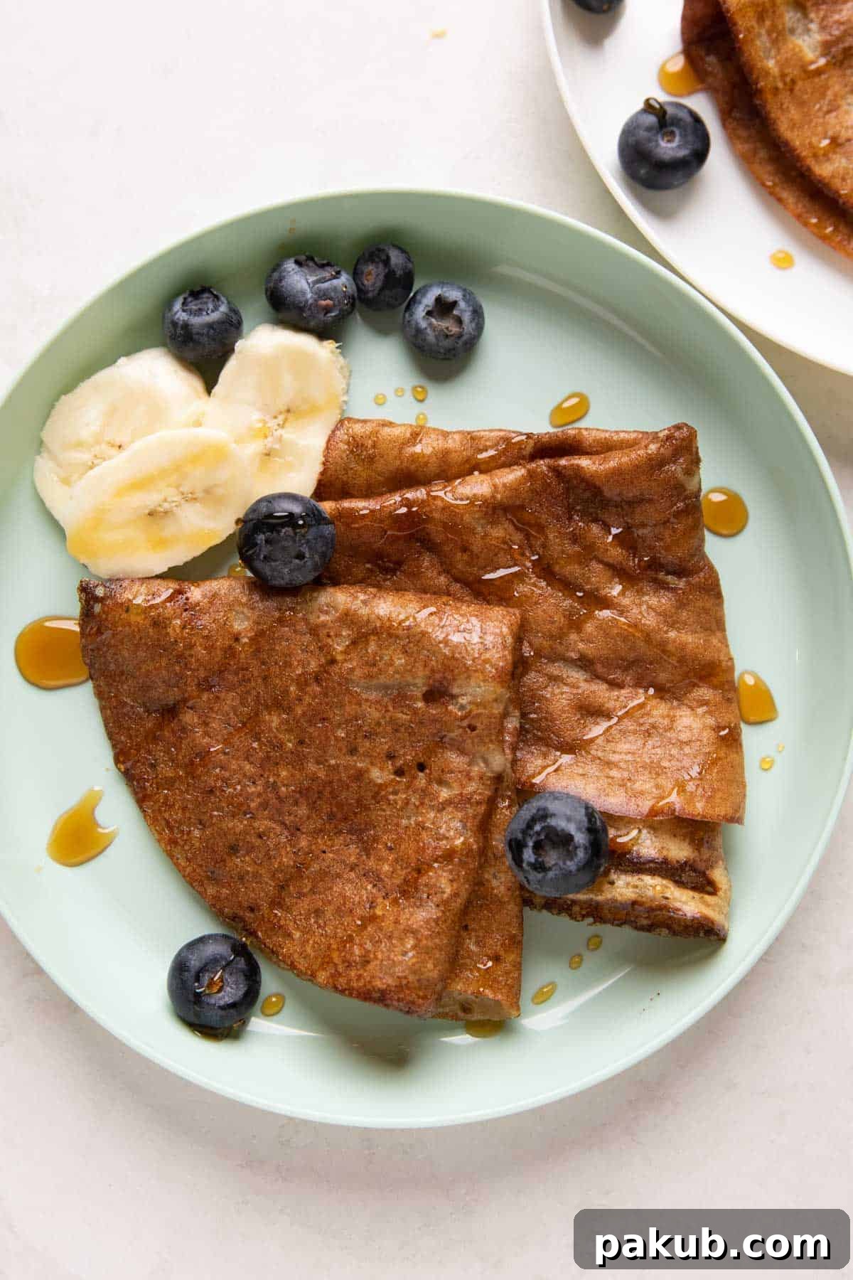 Banana Dosa served on a green kids plate with fresh banana slices, a side of honey, and vibrant blueberries, making it a complete and appealing meal.