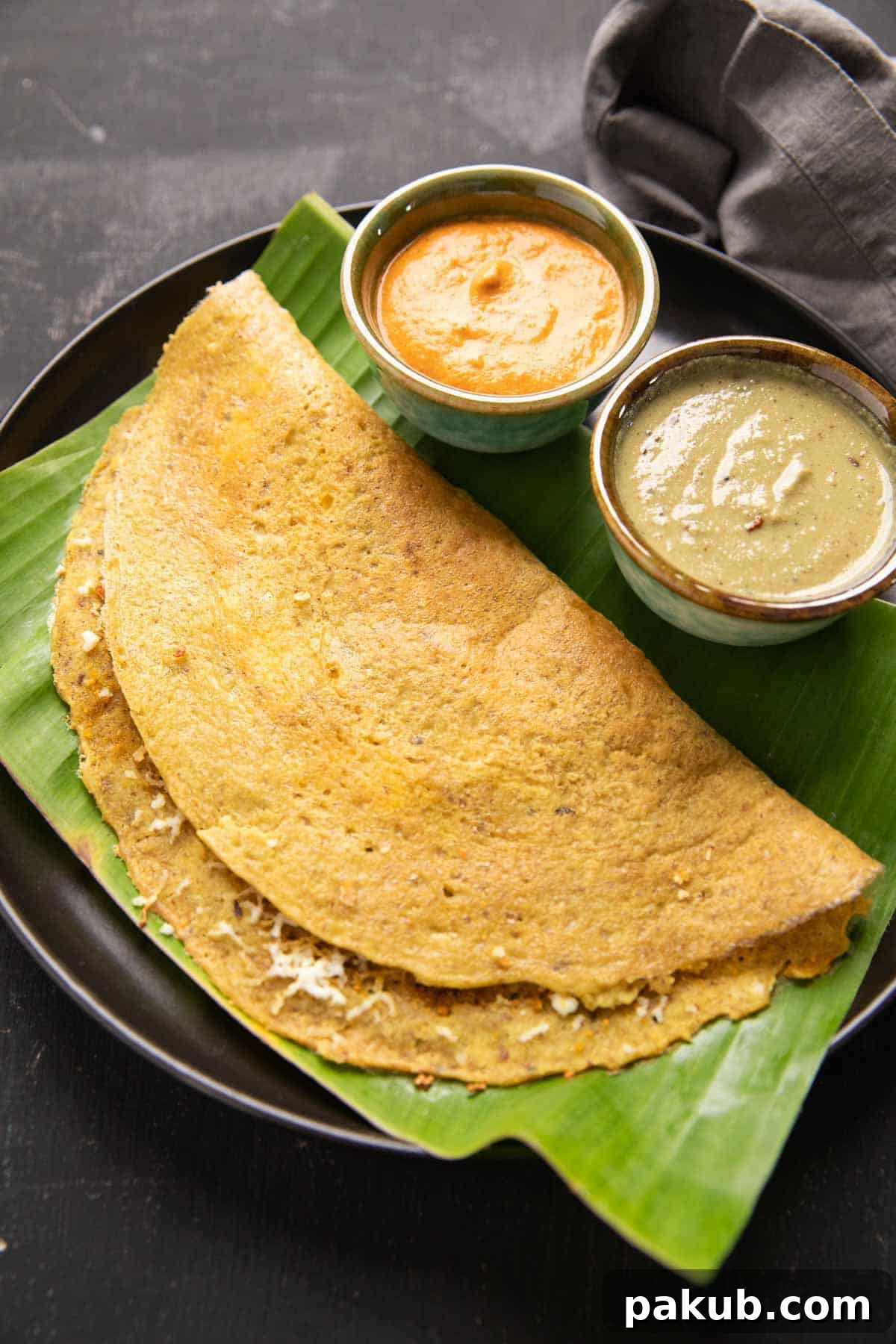 A beautifully plated High Protein Dosa on a traditional banana leaf, accompanied by an assortment of delicious chutneys and a rich curry, showcasing a complete and inviting meal.