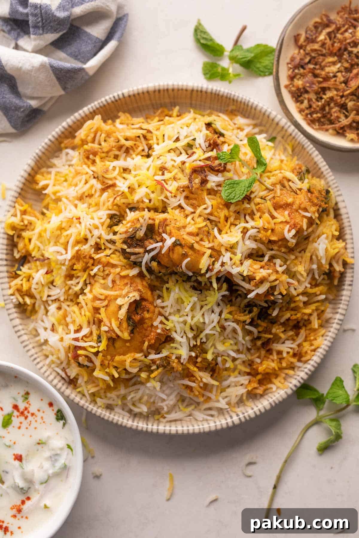 Elevate Your Biryani 19 Essential Tips 2 A beautifully presented plate of Chicken Biryani, garnished with crispy fried onions, fresh mint, and coriander, served alongside a refreshing raita.