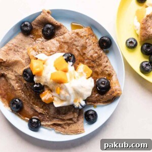 Ragi Crepes served on a plate topped with whipped cream, mango and blueberries