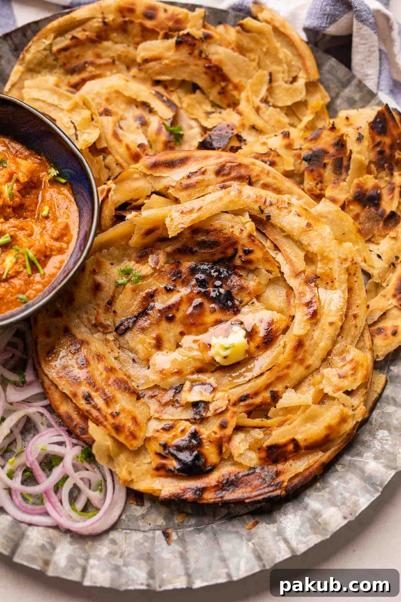 Lachha Parathas served on a plate with curry and onions, showcasing their beautiful golden layers.