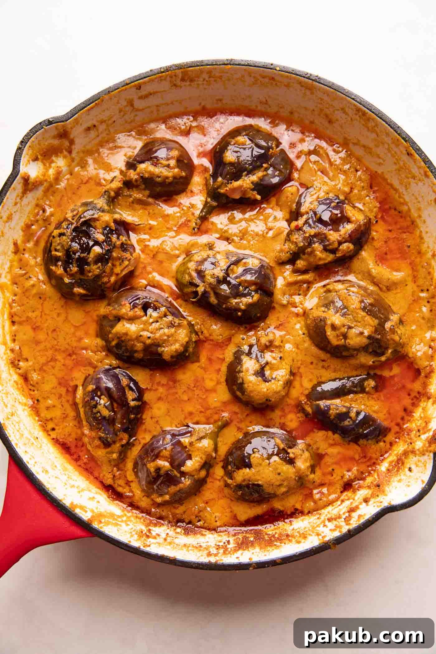 Picture of stuffed brinjal curry in a vibrant red enamel pan, garnished with fresh cilantro.