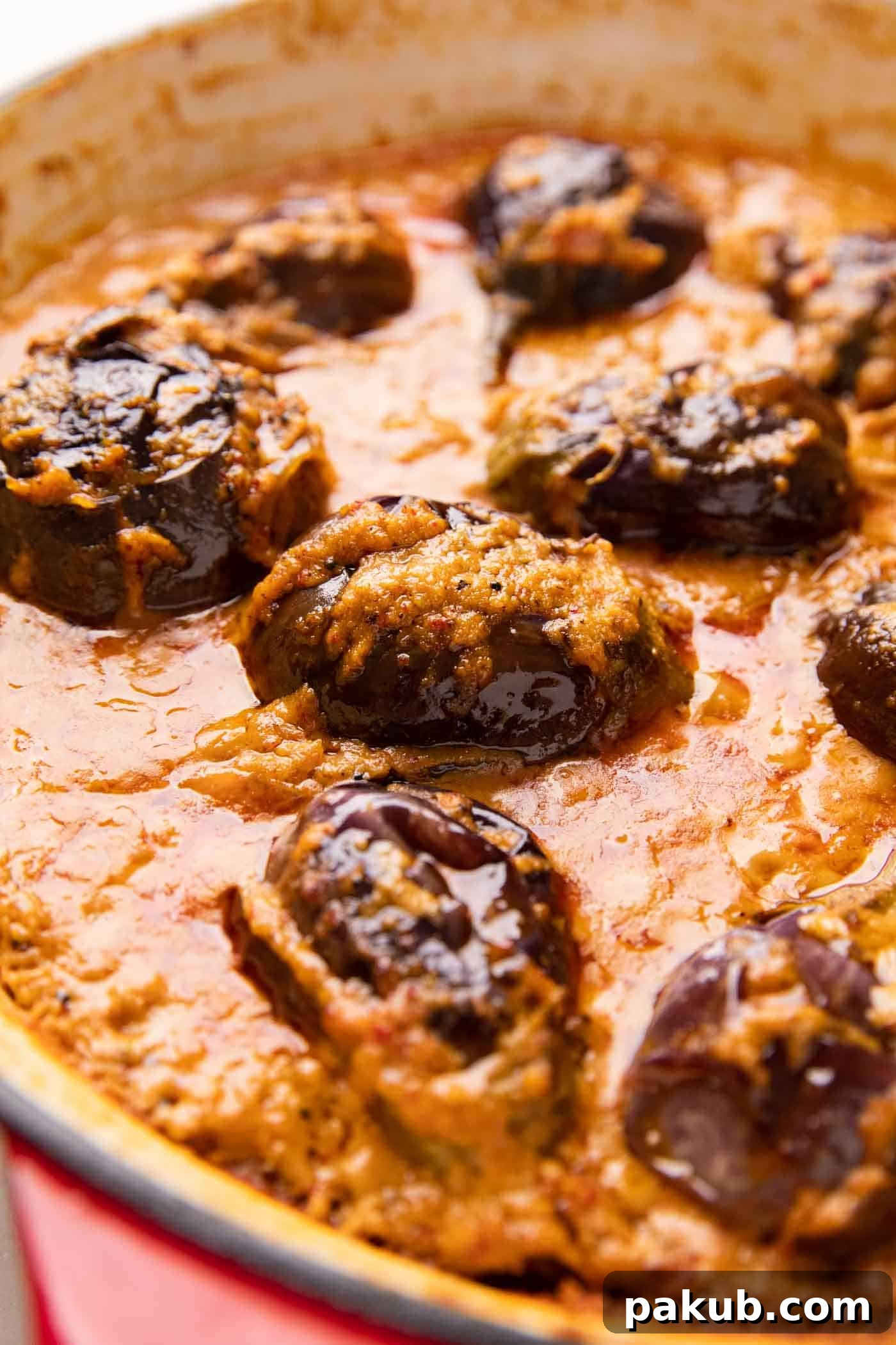 A close-up shot of a tender stuffed brinjal submerged in the rich, thick gravy of the curry, highlighting its texture and deep color.
