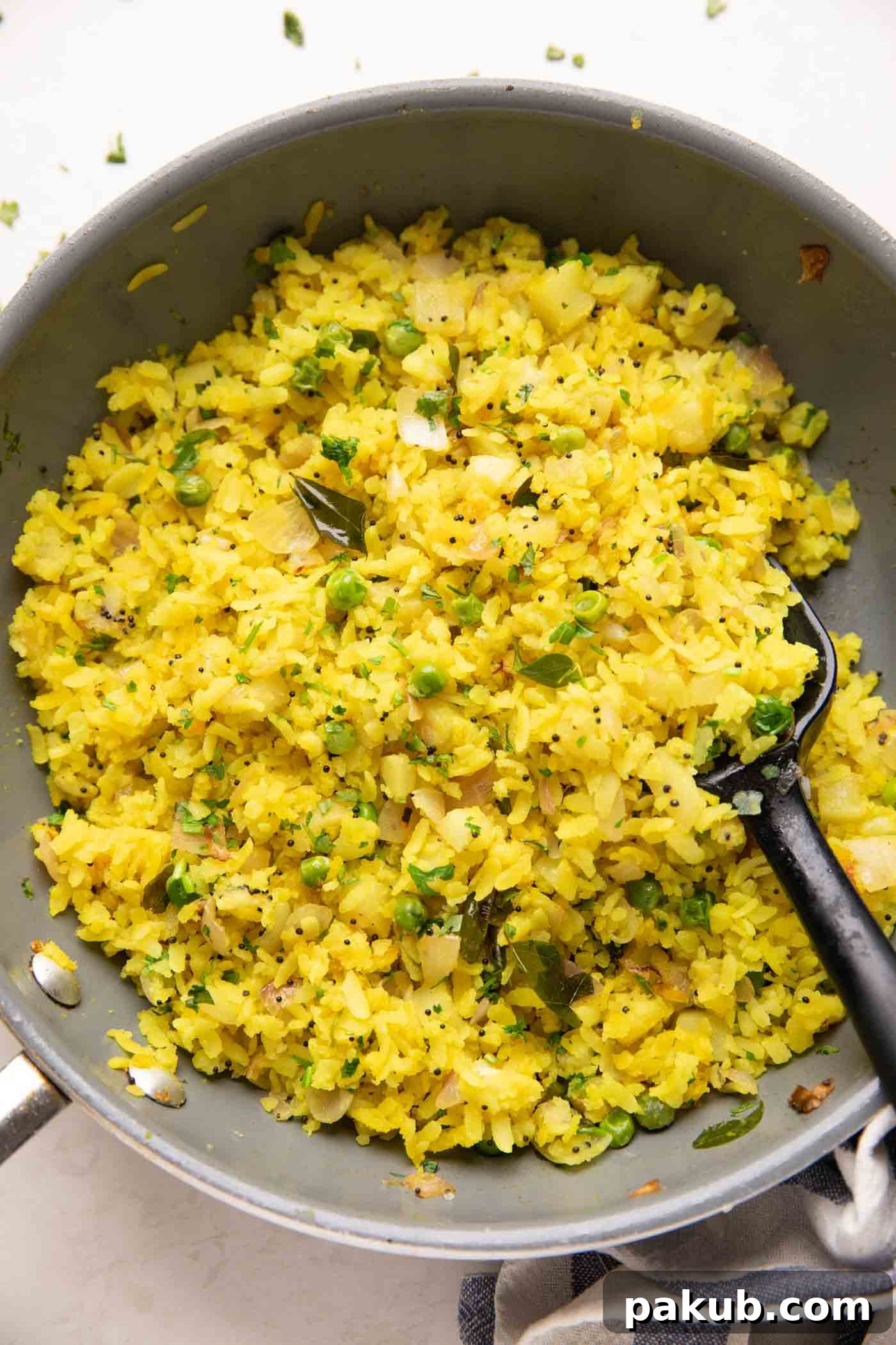 Spiced Onion Potato Poha 2 Freshly cooked Kanda Batata Poha in a traditional Indian pan (kadhai), garnished with coriander leaves and a squeeze of lime