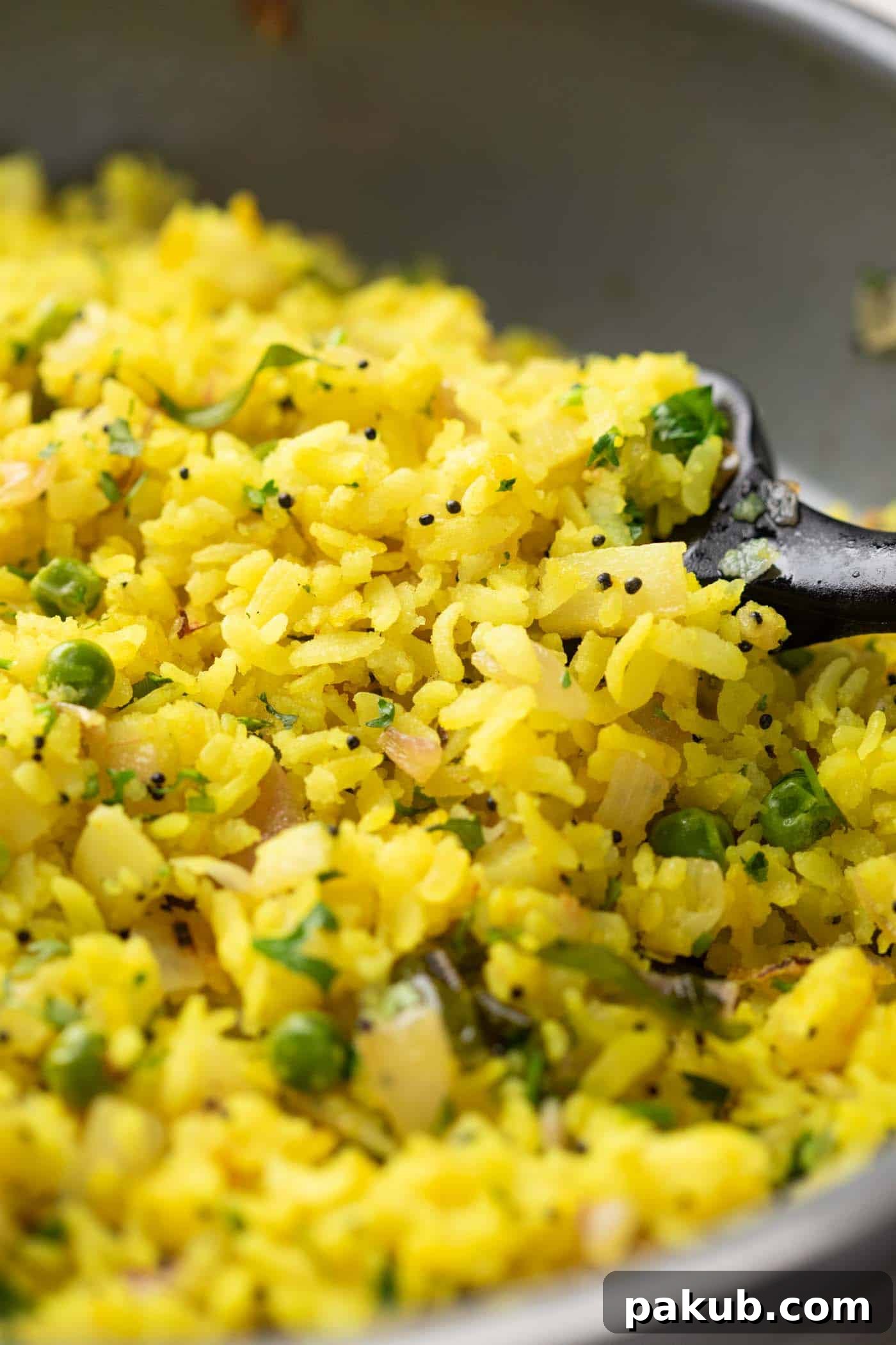 Spiced Onion Potato Poha 7 A close-up view of the fluffy and perfectly textured Kanda Batata Poha, showcasing its vibrant color and garnish of fresh coriander and lime