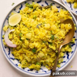 Spiced Onion Potato Poha 8 A bowl of Kanda Batata Poha garnished with fresh coriander, sliced onion, and a lime wedge on the side, ready to be served