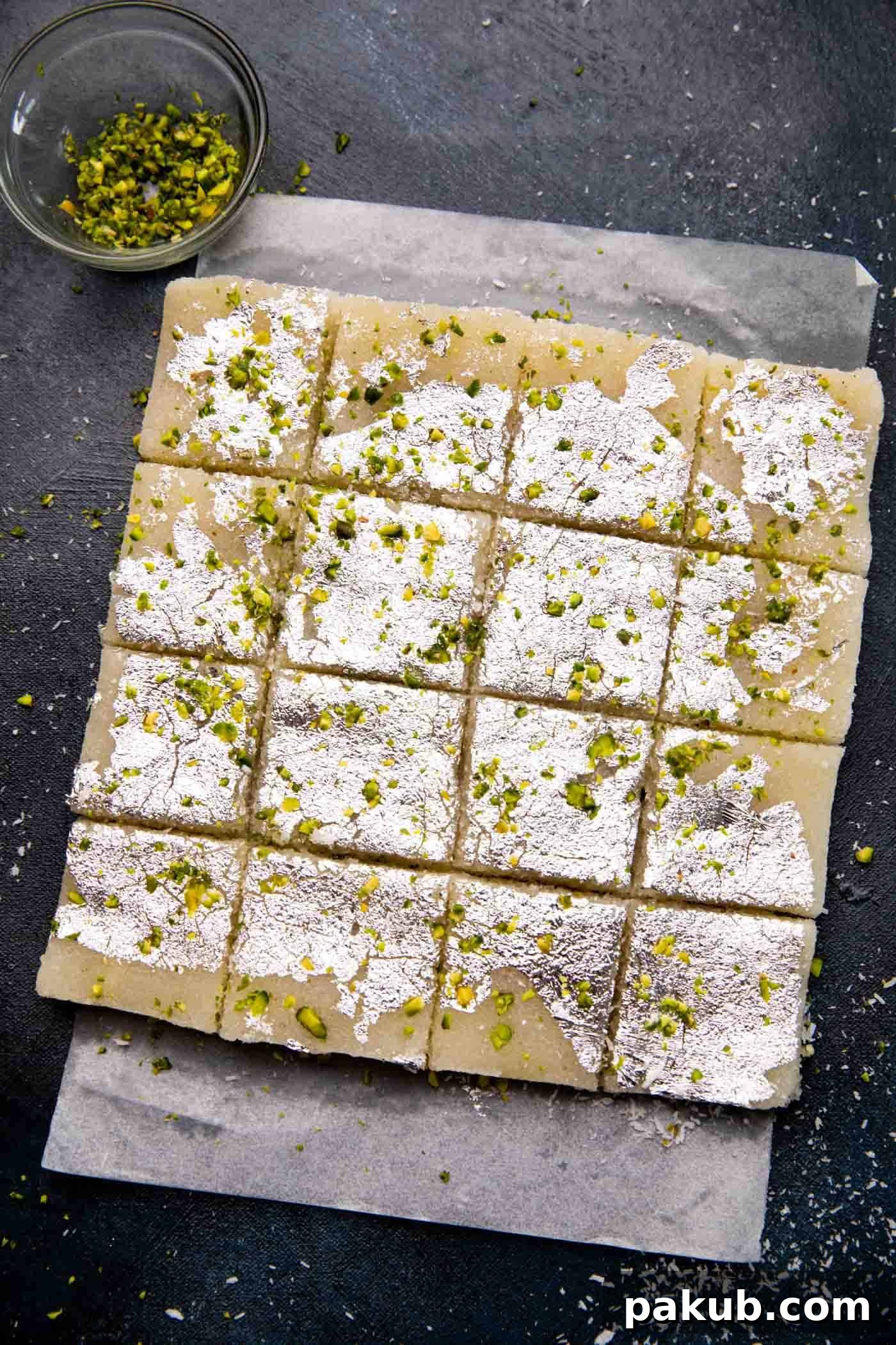 Sweet Coconut Fudge 2 Sliced Coconut Barfi (Nariyal Barfi) arranged neatly on parchment paper, showcasing its soft texture and pristine white color, often garnished with pistachios.
