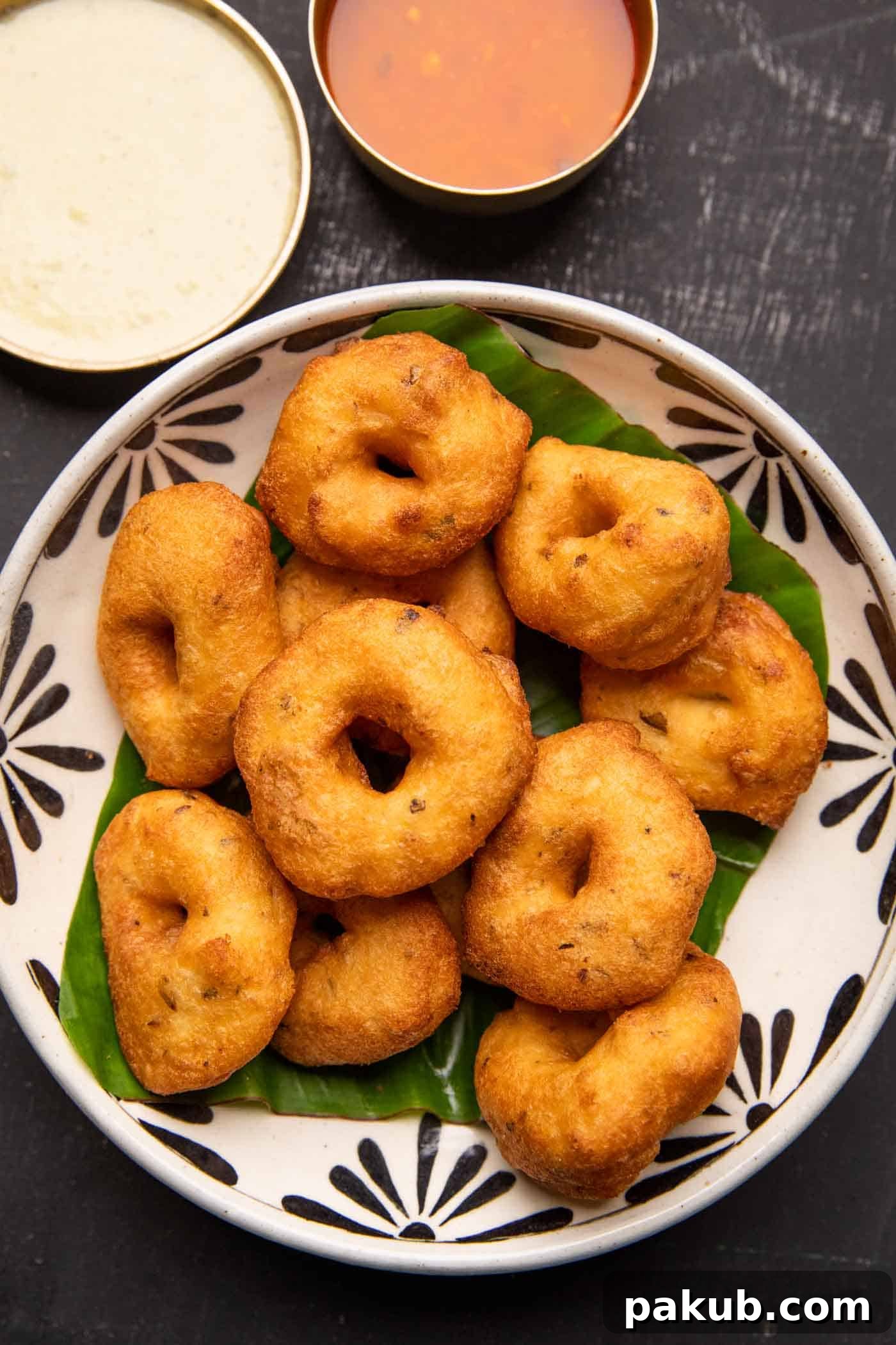 Medu vada served over a banana leaf in a bowl with chutney and sambar on the side