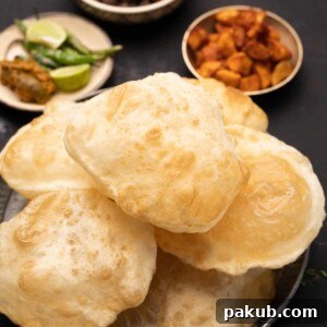 A plate of stacked bhature with a side of fried chili, fried aloo, and chole, presenting a hearty meal