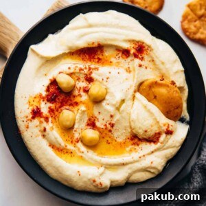 Classic Hummus served beautifully on a plate with fried pita, olive oil, and chickpeas.
