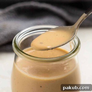 Creamy Thai Peanut Sauce Salad Dressing in a jar, with a spoon taking a scoop.