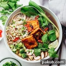 A vibrant bowl of vegetarian pho soup generously topped with a variety of fresh ingredients.