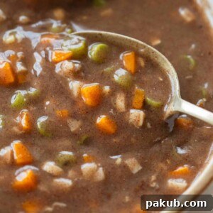 A wholesome white bowl of ragi soup, featuring diced carrots and beans, accompanied by a spoon.