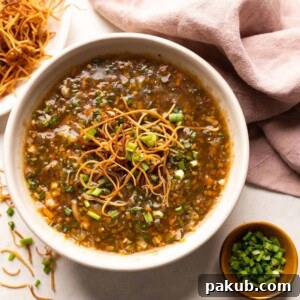 Homemade Chicken Manchow soup served in a white bowl, generously topped with crispy fried noodles and fresh spring onions.