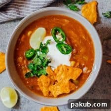 A hearty bowl of Chicken Enchilada Soup, made easily in the Instant Pot, and garnished with sour cream, cilantro, sliced jalapeños, tortilla chips, and a fresh lime wedge.