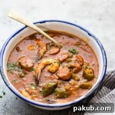 A robust New Orleans Shrimp Sausage Gumbo, served beautifully in an enamel bowl with a spoon, inviting you to taste its rich flavors.