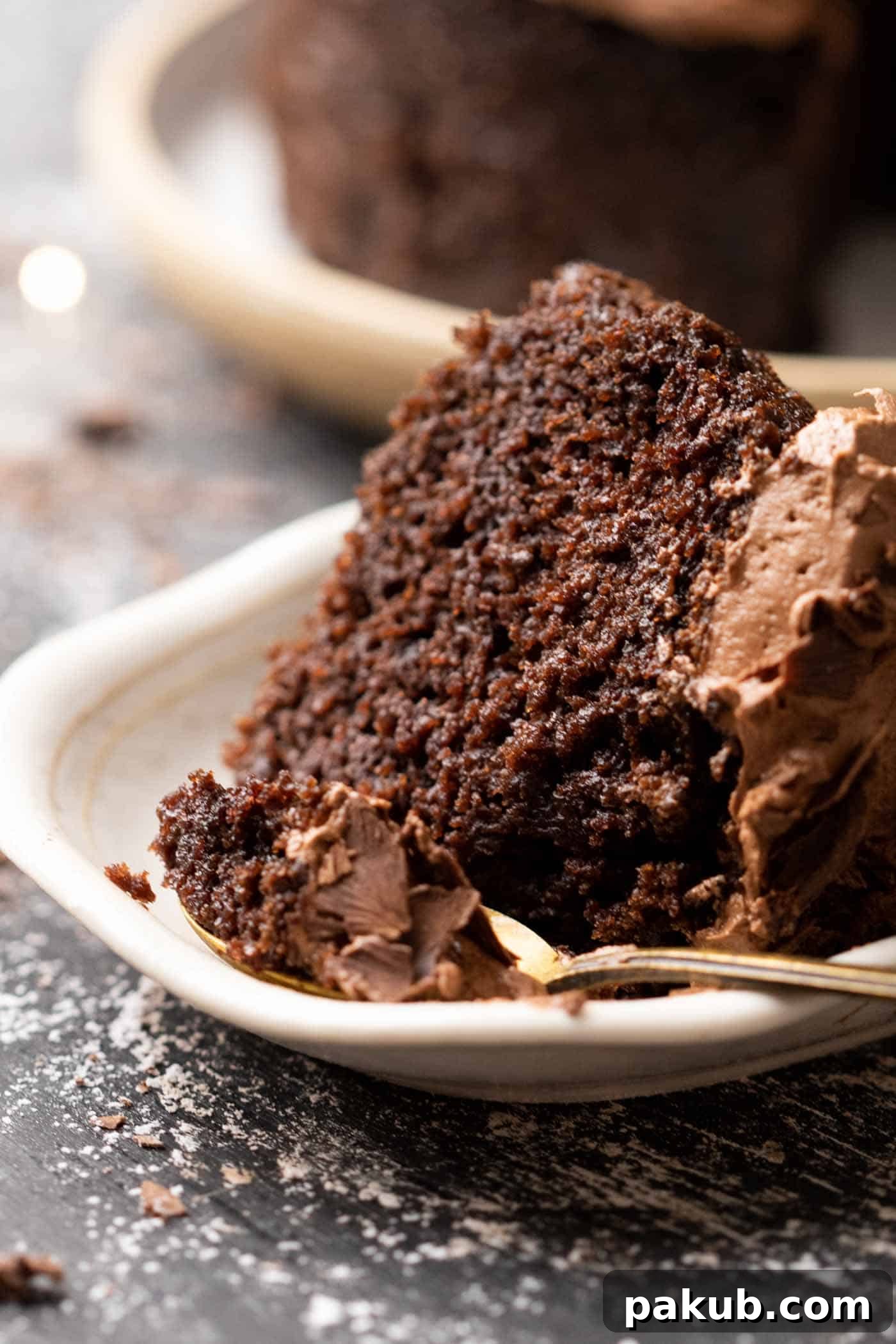 A close-up shot of a perfectly sliced chocolate cake, adorned with chocolate buttercream and a spoon, highlighting its moist and rich texture.