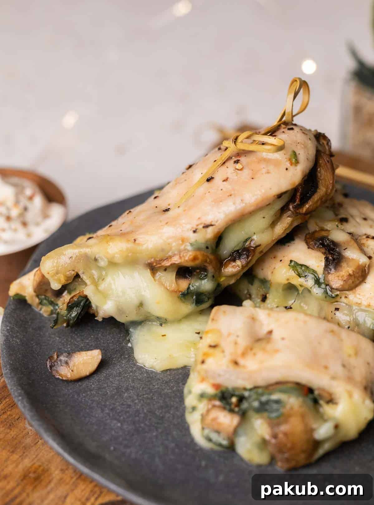 Golden Air Fryer Stuffed Chicken Breasts 7 A perfectly cooked stuffed chicken breast, sliced to reveal the cheesy mushroom and spinach filling, served on a dark grey plate with fresh herbs.