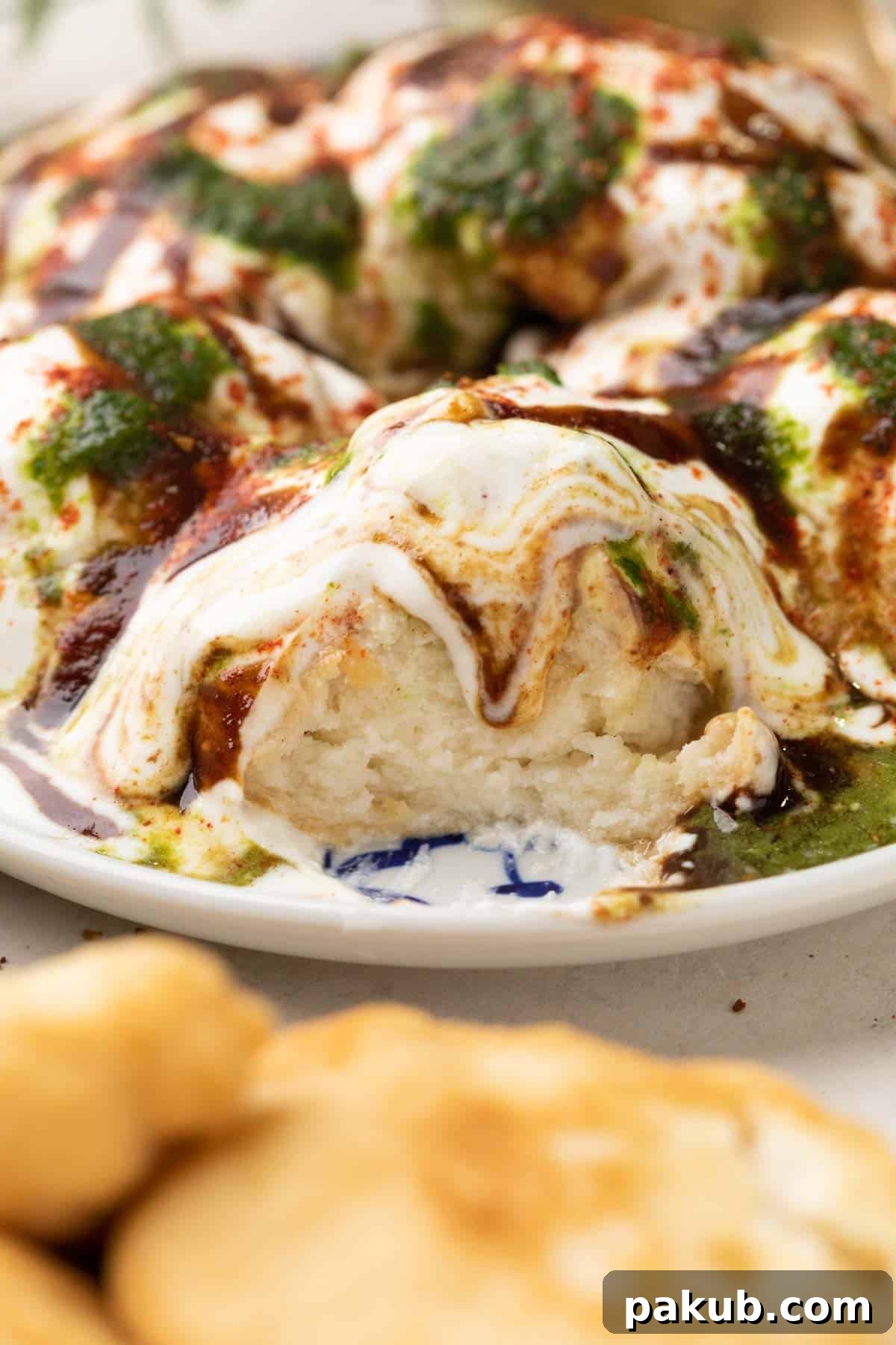 Cloud-Soft Lentil Fritters in Spiced Yogurt 2 Close up of a cut piece of dahi vada showing the soft interior, garnished with chutneys and spices