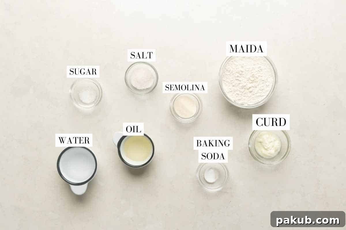 A beautifully composed shot of all the essential ingredients laid out for making bhatura: all-purpose flour, salt, sugar, baking soda, curd, semolina, water, and oil.