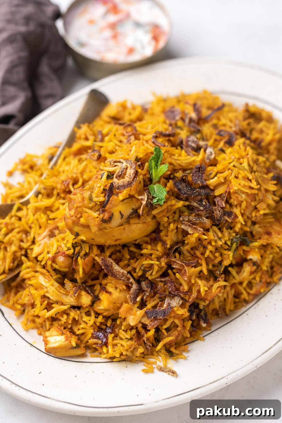 Aromatic Instant Pot Chicken Biryani 2 A white plate full of flavorful Instant Pot Chicken Biryani with a side of refreshing raita, garnished with fresh herbs and crispy onions.