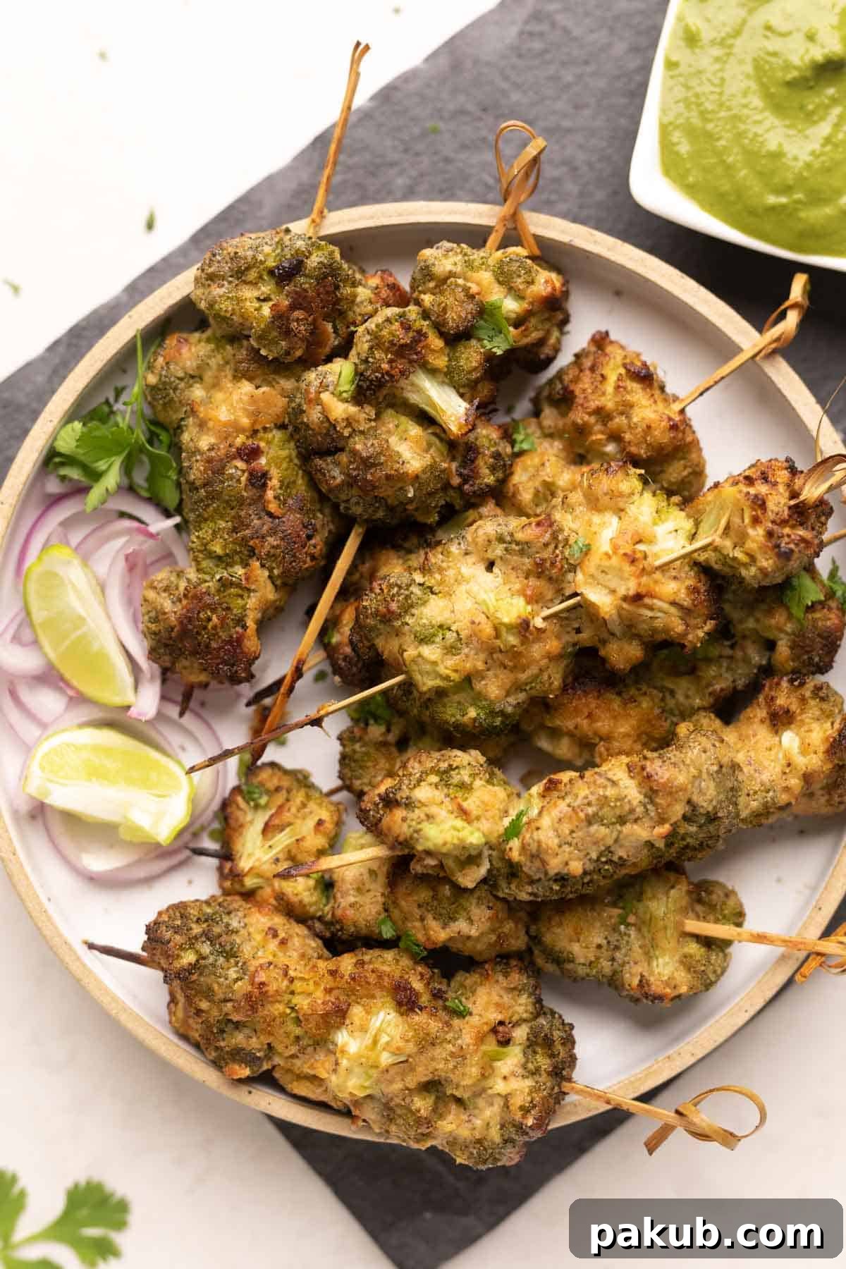 Air-Fried Malai Broccoli 2 A vibrant plate of Malai Broccoli on skewers, accompanied by thinly sliced red onion and a refreshing green mint chutney, ready to be served as an irresistible Indian appetizer.