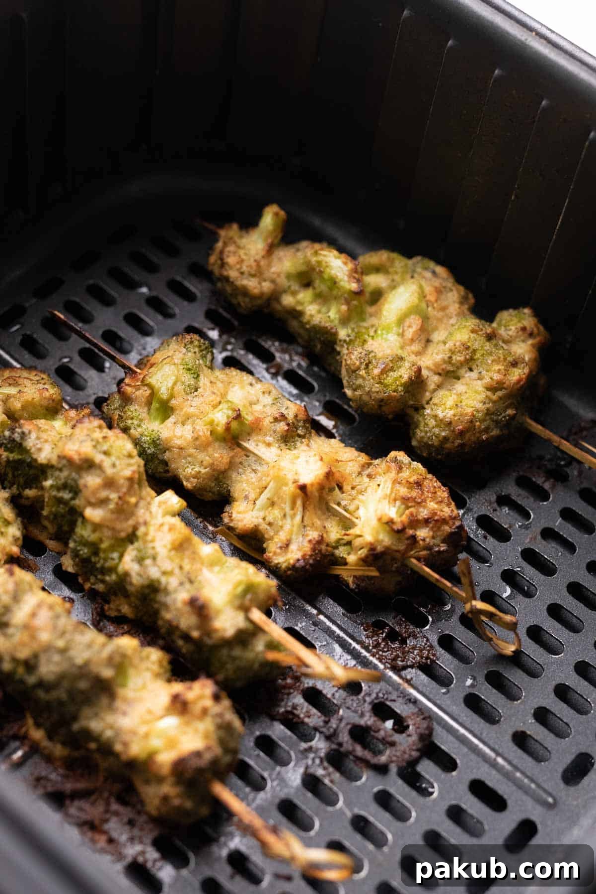 Air-Fried Malai Broccoli 7 Close-up shot of perfectly cooked Malai Broccoli on skewers, displayed beautifully in an air fryer basket, showcasing its lightly charred exterior and creamy coating.