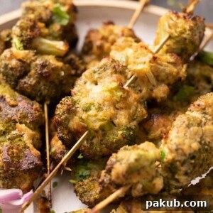 A close-up shot of succulent Malai Broccoli florets on skewers, beautifully presented on a plate, highlighting their creamy coating and golden-brown char.
