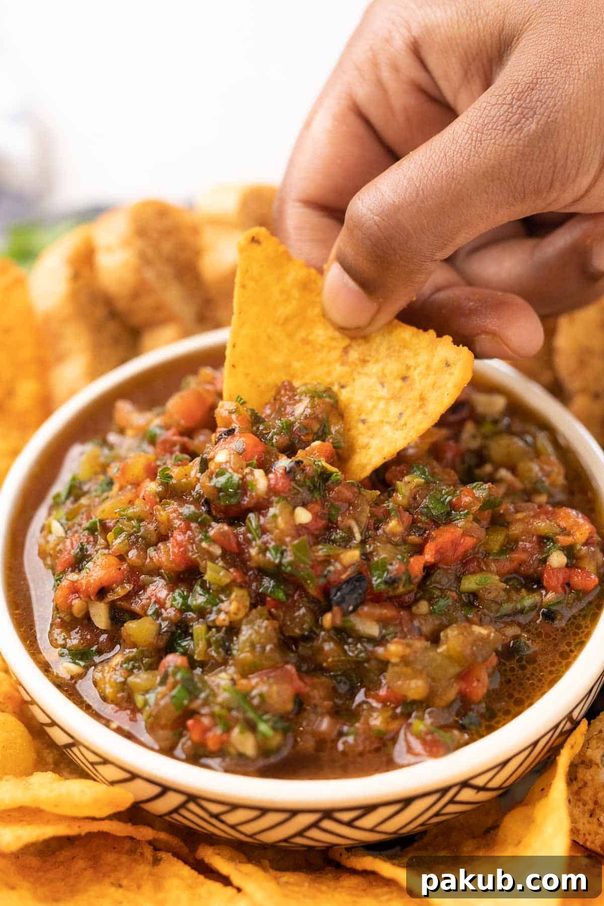 Fire-Roasted Salsa 6 A nacho chip being dipped into a bowl of roasted tomato salsa, showcasing its texture and deliciousness.