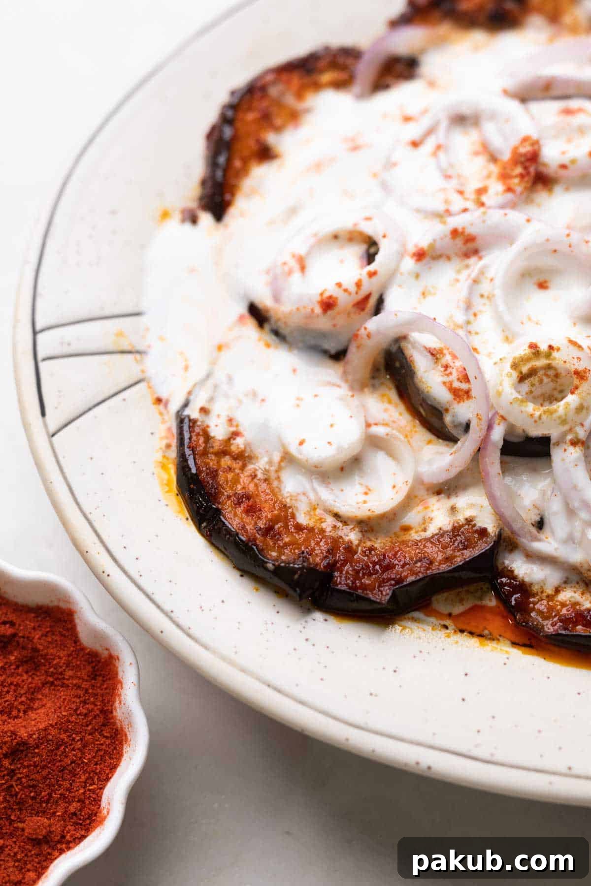 Close up of platter with fried eggplant slices and sliced onion topped with a curd mix