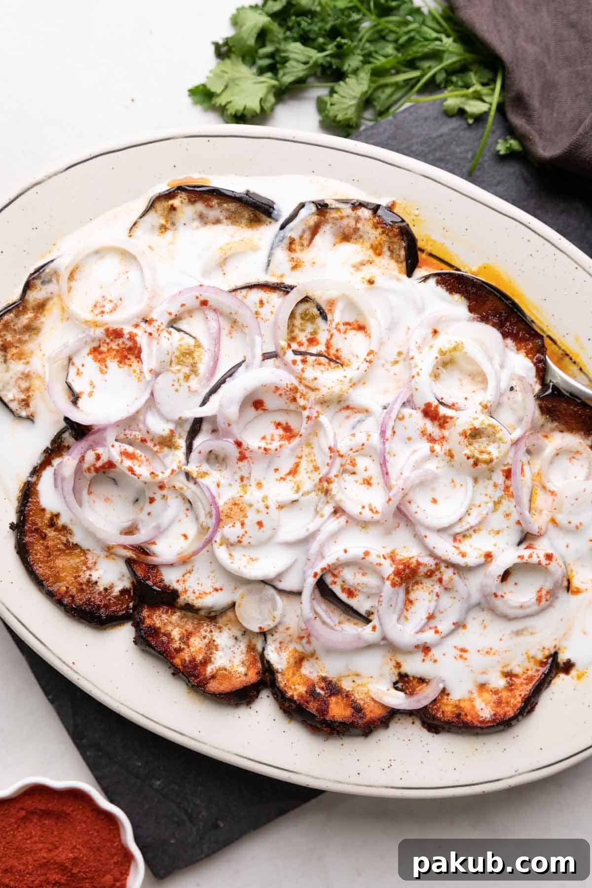 Platter with fried eggplant slices and sliced onion topped with a curd mix