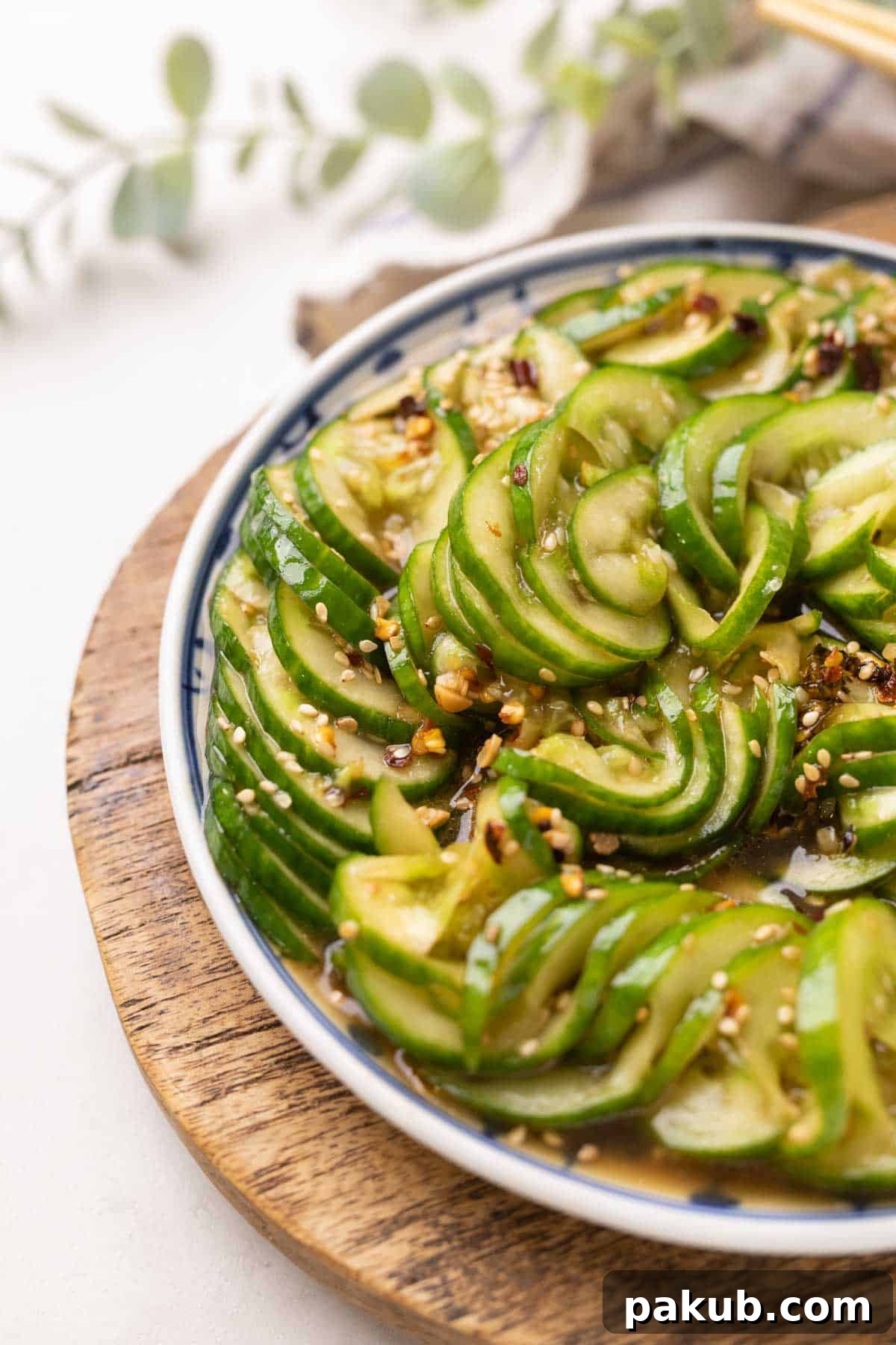 Sesame Garlic Cucumber Salad 2 Vibrant Asian cucumber salad served on an elegant blue and white plate, resting on a rustic brown wooden board, ready to be enjoyed.
