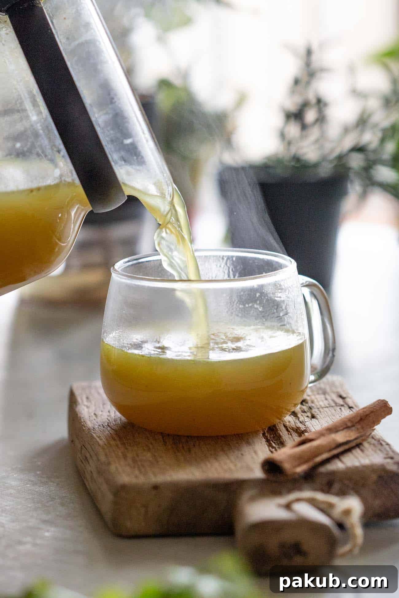 Liquid Gold Chicken Broth 2 A warm, golden shot of turmeric chicken bone broth being poured into a clear glass mug resting on a rustic wooden board, evoking comfort and healing.
